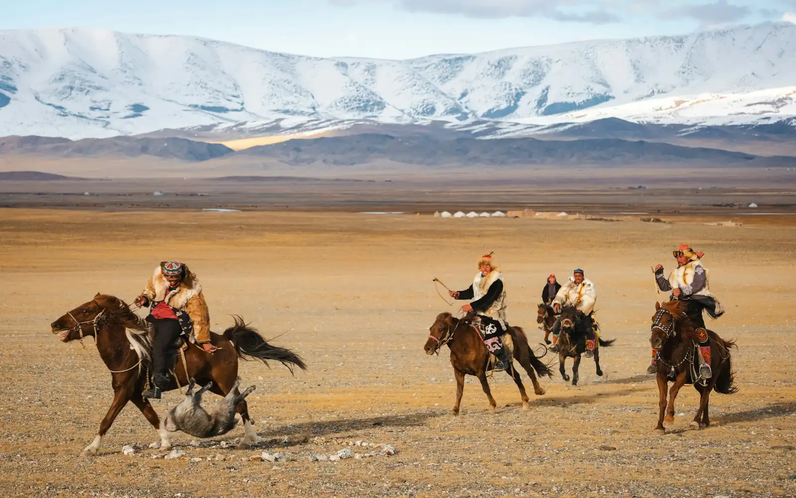 Riders crossing the steppe below snowy peaks