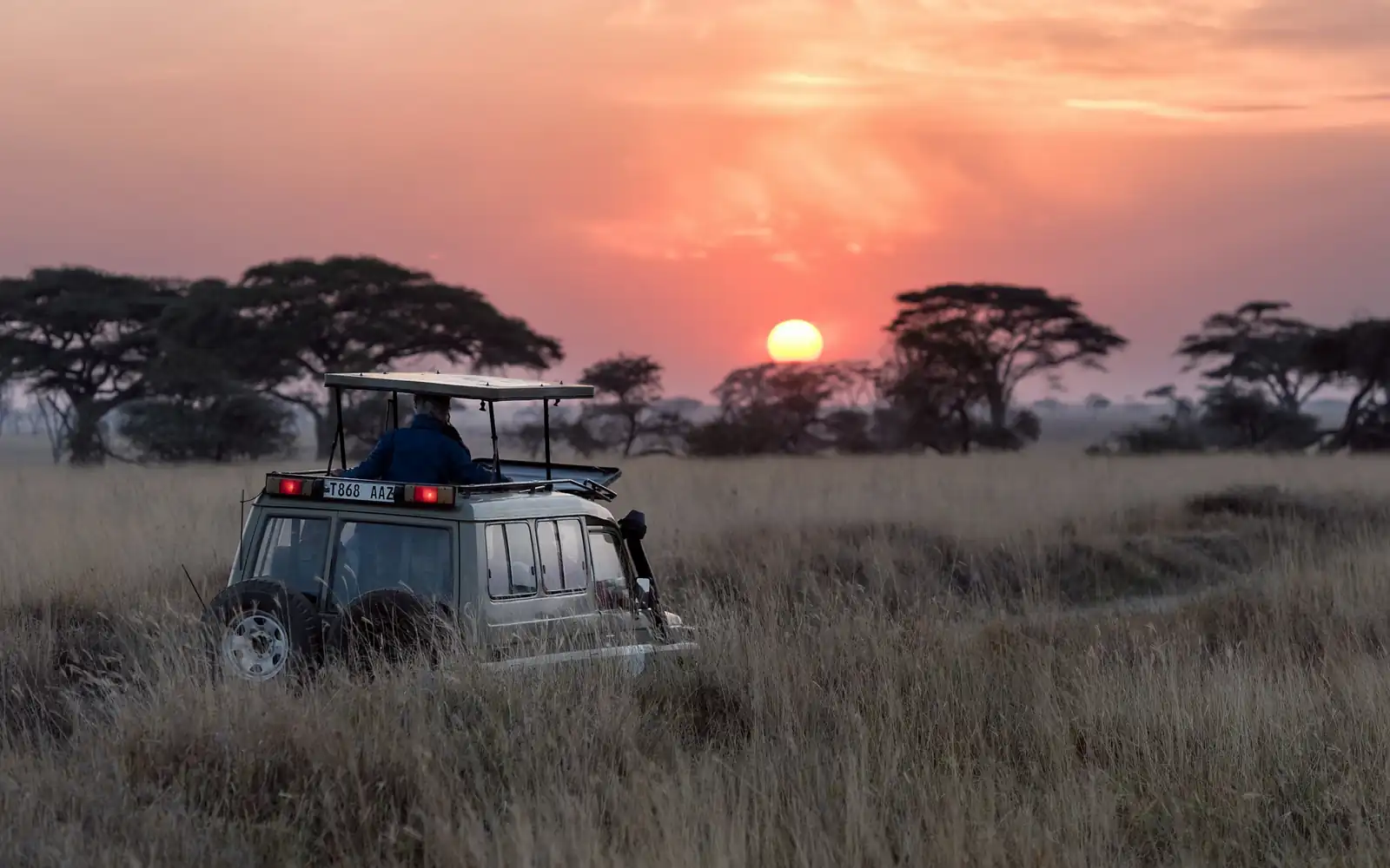 A safari vehicle at sunset on the open plains
