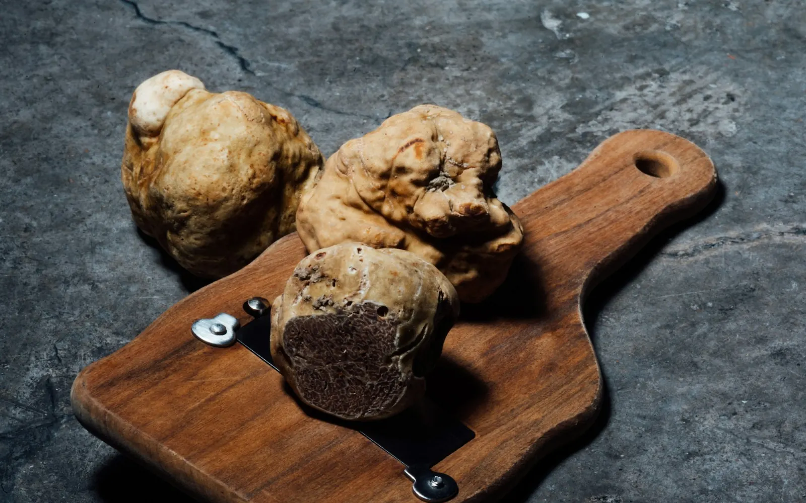 Whole white truffles on a wooden board with a slicer